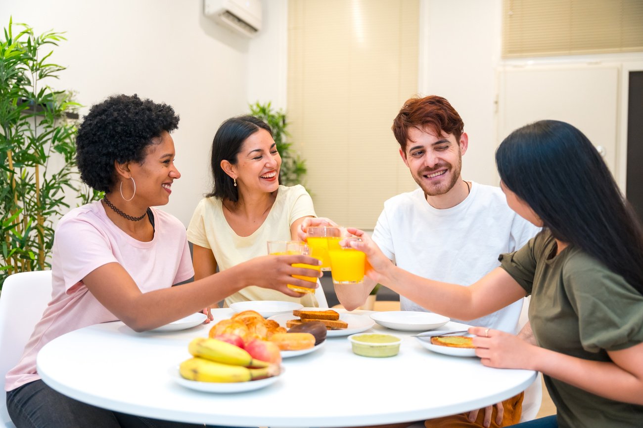 Multicultural friends toasting with juice eating healthy breakfast at home